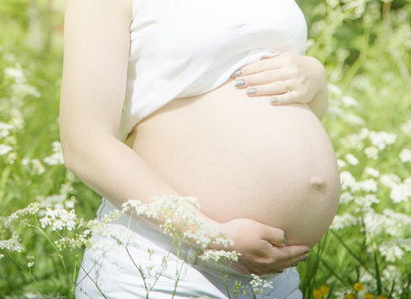 pregnant woman's belly in an outdoor setting illuminated by the sun raysの写真素材