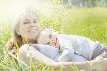 The little boy pressed his lying hugging pregnant mom in the meadowの写真素材