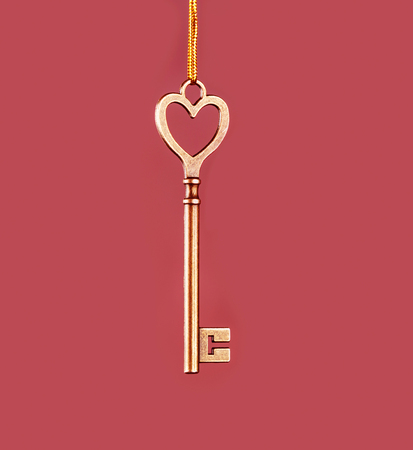 Golden key to hanging on a golden thread on a pink backgroundの写真素材