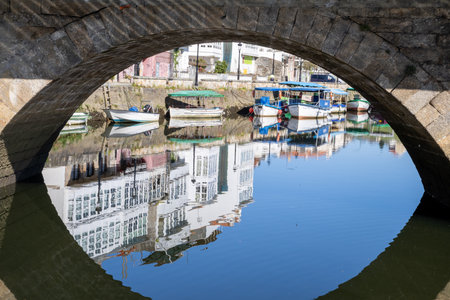 Traditional Galician white buildings seen from Ponte Vella bridge over Mandeo River in Betanzos, Spain, surrounded by lush greenery.の写真素材