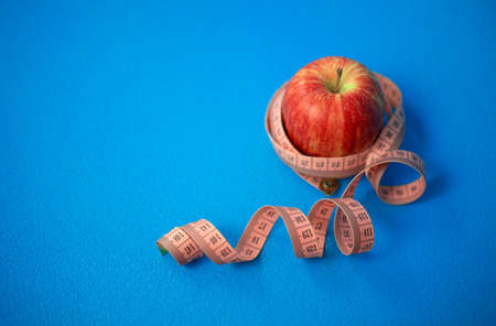 One apple a day for your health. Red apple with centimeter tape on a blue background.