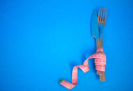 The fork and knife are wrapped in pink measuring tape on a blue backgroundの写真素材