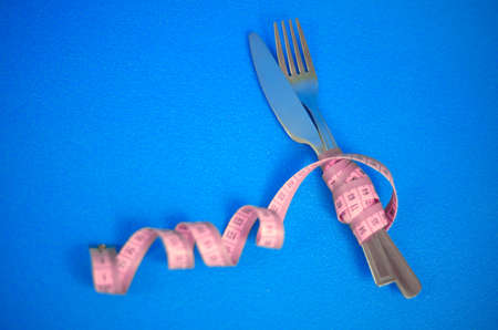 The fork and knife are wrapped in pink measuring tape on a blue backgroundの写真素材