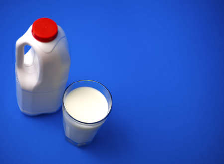 Airtight one gallon milk jug with a red cap and full glass milk on blue background