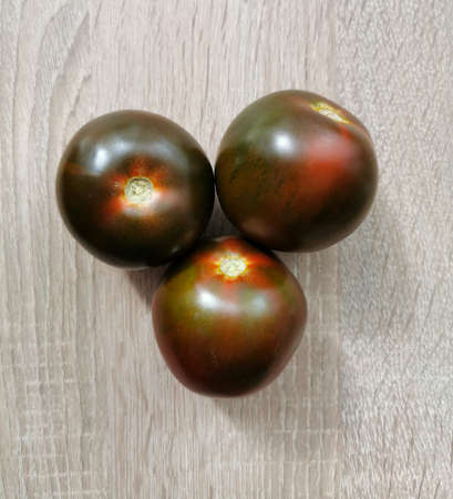 Three fresh, dark red heirloom tomatoes on a wooden tableの写真素材