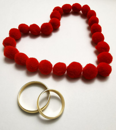 Gold wedding rings and red heart. Wedding rings on the white background, surrounded by the heart. Symbol of love and devotionの写真素材