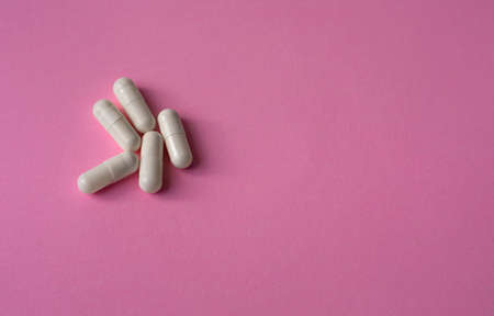White, large capsules, pills or tablets on a pink background