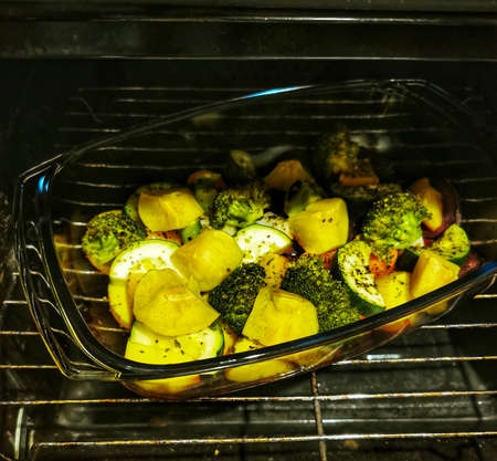 Tasty and colored vegetable mix with spices and olive oil. Baked vegetables in the oven. Potatoes, broccoli, beets, zucchini, carrots, apples in a glass bowlの写真素材