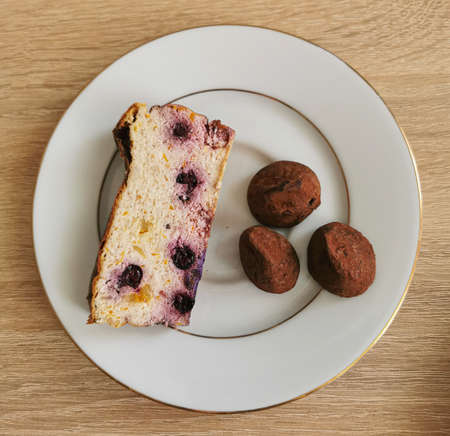 A piece of homemade cheesecake with blueberries and three sweet truffles on a white plateの写真素材