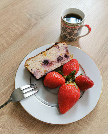 A piece of homemade cheesecake with blueberries, strawberries on a white plate and coffee