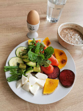 A healthy breakfast rich in protein, fats and carbohydrates. Oatmeal with nuts, soft-boiled egg, mocarella cheese, colorful vegetables, green leaves of mint, parsley and onionの写真素材