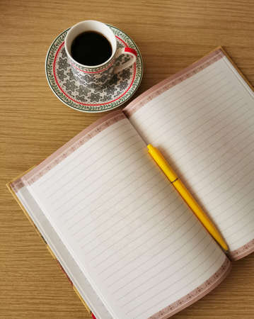 Writing paper, a cup of coffee and a pen resting on a notepad on a wooden desk