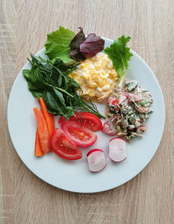 A healthy and balanced breakfast. Scrambled eggs, tomato, carrot, radish, salad, green leaves of fresh vegetablesの写真素材