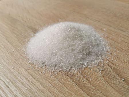 Pile of granulated white sugar on wooden table