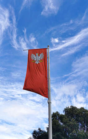 The state flag of Poland with the emblem of the Republic of Poland, waving in the wind on the left on blue sky background. 02/08/2021 Warsaw, Polandのeditorial素材