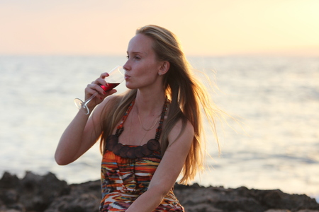 A beautiful woman sitting on the beach and drinking wine.の写真素材