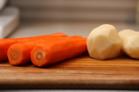 Peeled potatoes and carrots on wooden chopping board.の写真素材