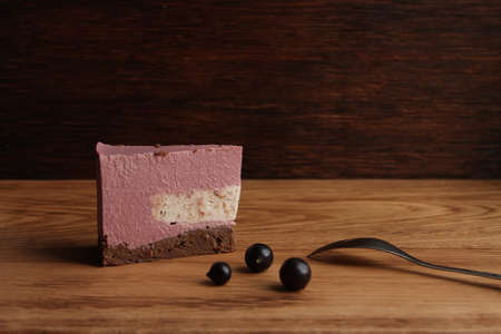 A piece of homemade mousse sweet pink cake with several black currant on the wooden board