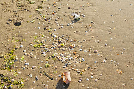 Plastics and other rubbish on the shore of a beach mixed with the sand and shells of the sea causing pollution to the environmentの写真素材