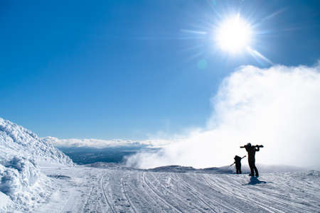 Are, Sweden - March 11, 2019: Two skiers walk down with the skis on the men on top of ?? Reskutan on a sunny day with low clouds in ?? Re, Swedenのeditorial素材