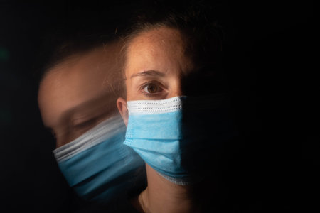 Dark portrait of a serious woman with only half her face lit up on a black background looking sad or...