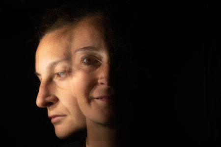 Dark portrait of a smiling woman with only half her face lit up on a black background that unfolds into another blurred face with a sad or depressed gesture.の写真素材