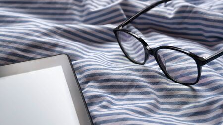 Editable or custom e-reader with glasses background on the bed in a sunny a peaceful morning