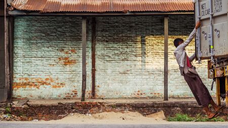 Young Burmese man hanging in at the back of a truck while driving on an empty and dirty Yangon streetの写真素材