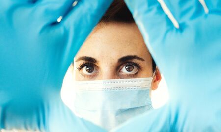 Woman wearing a blue medical mask and latex gloves holding her hand in front of her face
