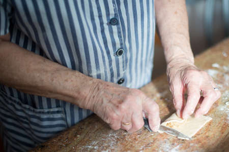Typical Asturian Christmas dessert, casadielles. Aged woman's hands putting the filling made of nuts on the homemade dough and cutting it with a knife. Gastronomyの写真素材