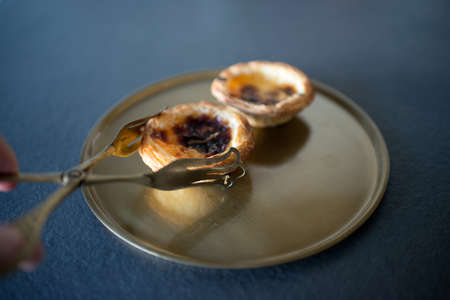 A hand using serving tongs to pick a delicious Belem cake (Pasteis de Belem), following Portuguese traditional recipe. Gastronomy.の写真素材
