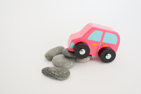 Toy pink car having problems with stones on the road. White background