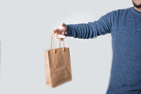 Young anonymous adult dressed with jeans and pullover delivering a brown paper bag. White backgroundの写真素材