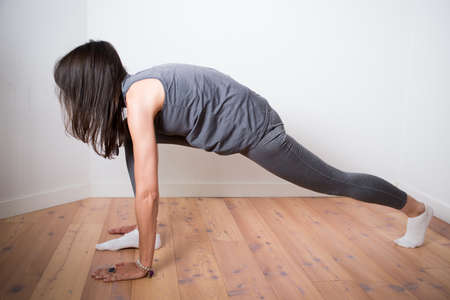 Woman during yoga practice at home dressed in gray. Low lunge pose. White backgroundの写真素材