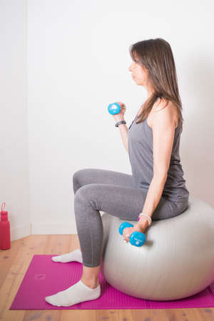 Caucasian attractive woman training at home with dumbbells and stability ball. White backgroundの写真素材