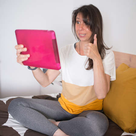 Attractive woman having a video chat at her bedroom. Agreement gesture, successの写真素材