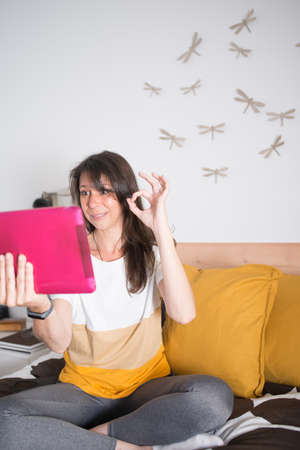 Woman 40-50 during a video chat at her bedroom. Left hand with success gesture, agreementの写真素材