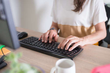 Close up of a woman working at home. Hands on the keyboard. White cup and a plant on the desk, next to herの写真素材