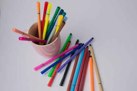 Pink cup with colorful markers and some others on a white surface. Copy space