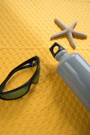 Summer concept, yellow background with sunglasses, water bottle and starfish
