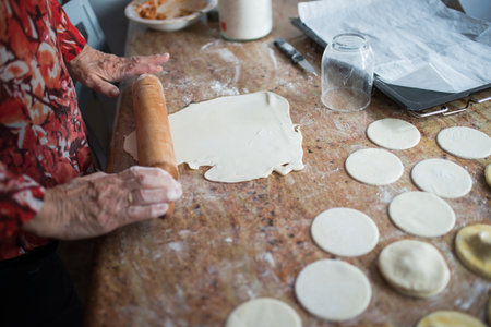Aged woman using a wooden rolling pin with puff pastry to make dumplings. View from above