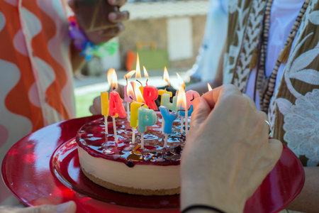 Caucasian hands lighting candles on a birthday cake. Cheese cake with strawberry jamの写真素材