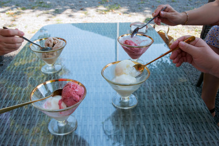 Friends enjoying ice cream desserts with golden spoonsの写真素材