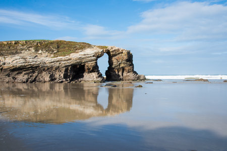 Natural arch at Catedrales beach, Lugo, Galicia, Spain. No people, sunny day. Beautiful reflectionの写真素材