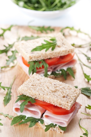 Sandwich with ham,tomato, and rucola salad on the wooden cutting boardの写真素材