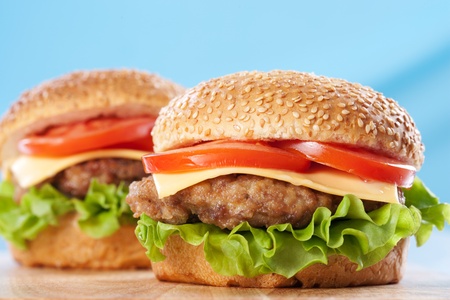Two cheeseburgers with tomatoes and lettuce on a wooden table with blue backgroundの写真素材