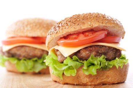 Two cheeseburgers with tomatoes and lettuce on a wooden table の写真素材