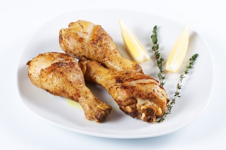 Roasted chicken legs with thyme and lemon on a plateの写真素材