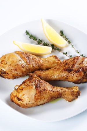 Roasted chicken legs with thyme and lemon on a plateの写真素材