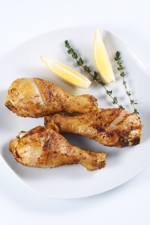 Roasted chicken legs with thyme and lemon on a plateの写真素材